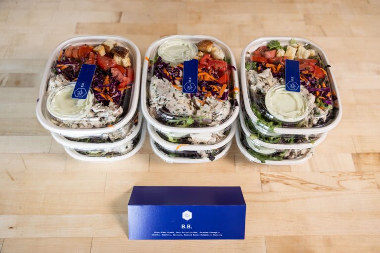 Multiple individual boxed salads stacked up with a placard of the menu item name.